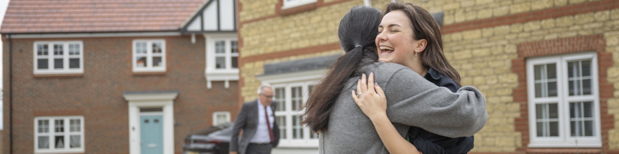 Two friends hug outside a house they've just purchased.